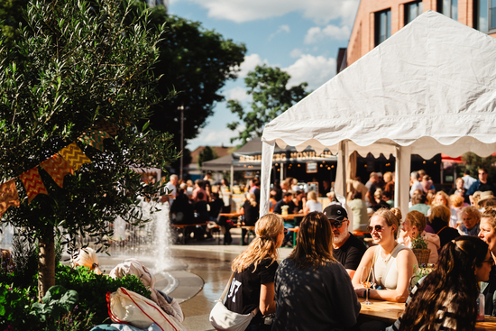 Rund um den Springbrunnen sitzen Menschen auf Bierbänken.